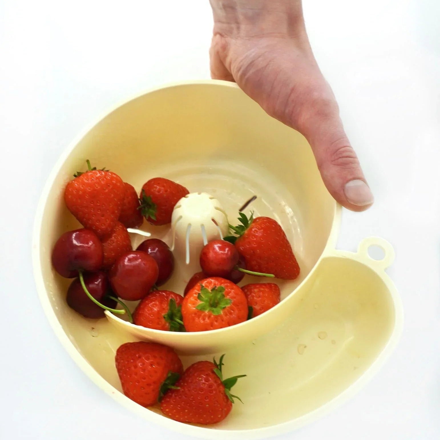 Hand holding a cream-colored juicer bowl with fresh strawberries and cherries