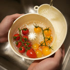 Red and yellow cherry tomatoes being washed in a plastic bowl under running water
